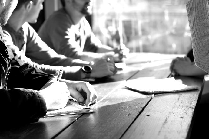 people sitting on chair in front of table while holding pens during daytime